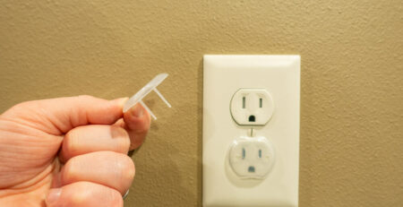 Parent baby-proofing their home by covering electrical outlet