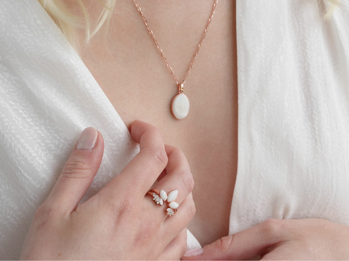 breastmilk jewelry oval simple necklace from keepsakemom in rose gold setting on light background with pearl powder in milk stone on model chest