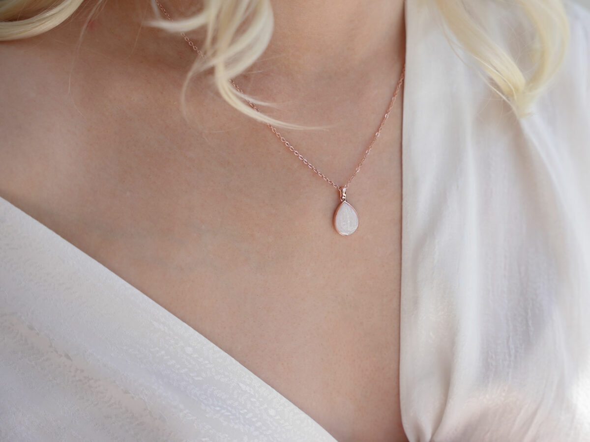 breastmilk jewelry teardrop pear shaped necklace in gold with opal flakes on a blonde model in white from keepsakemom