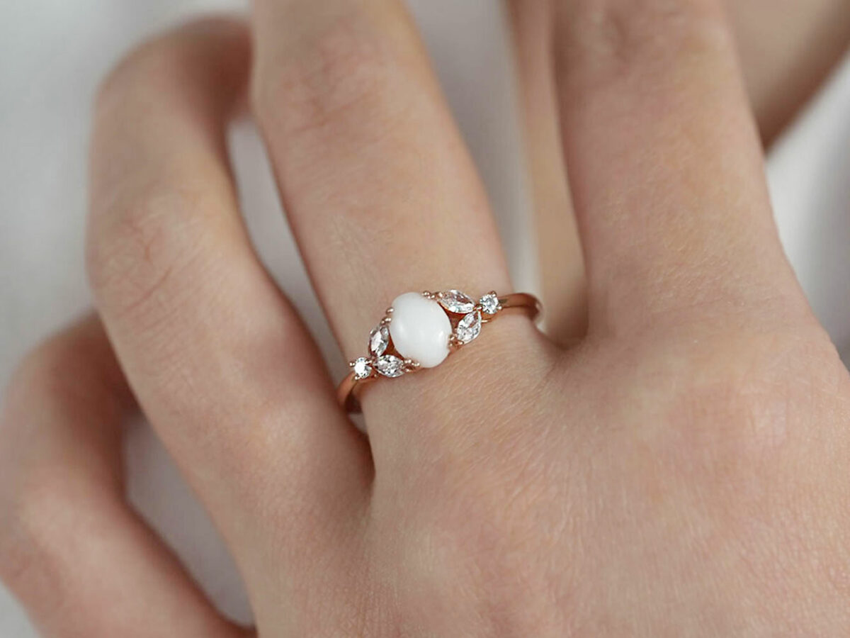 breast milk ring with oval stone and three clear crystals on each side in rose gold setting on a model hand