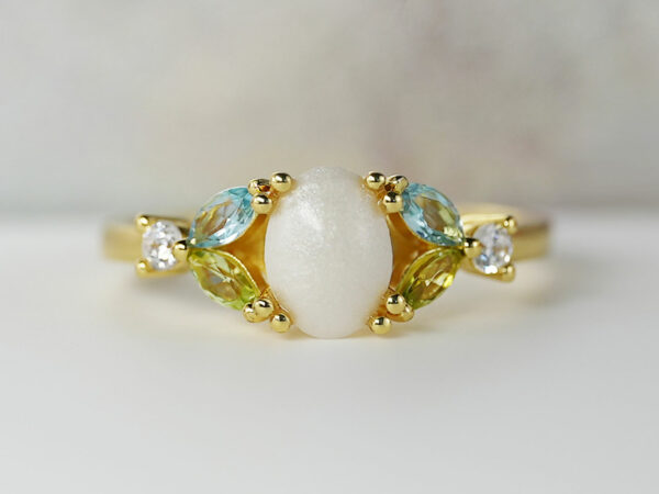 breast milk ring with oval stone and three crystals or gems on each side in aquamarine peridot and clear gem in gold setting from KeepsakeMom
