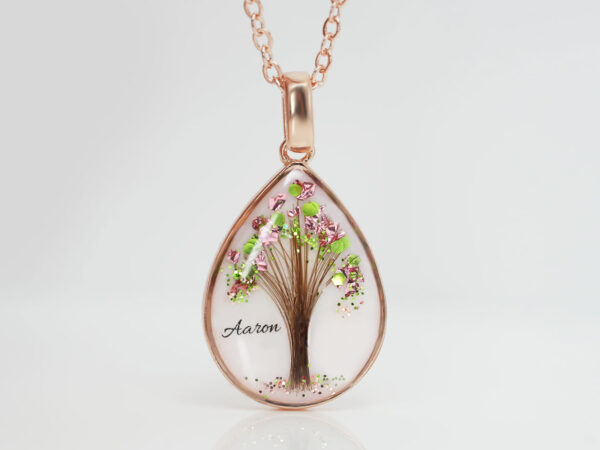 breastmilk jewelry teardrop pear shaped necklace with tree made with hair and green and pink flakes as leaves in rose gold on brown background from keepsakemom