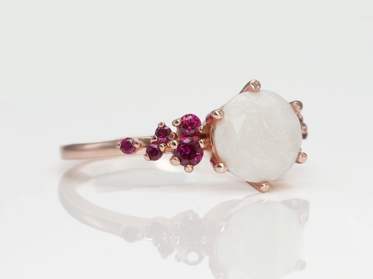 breast milk ring on a white background in rose gold and ruby red crystals on a side and central milk stone from keepsakemom