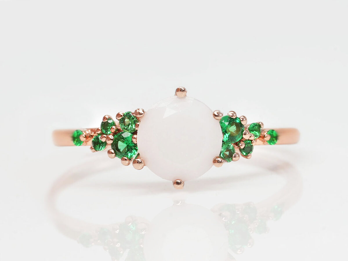 breast milk ring on a white background in rose gold and green emerald may crystals on a side and central milk stone from keepsakemom