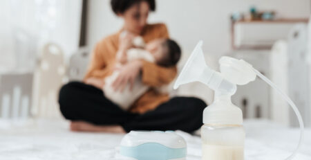Breast pump on bed in front of mom and baby