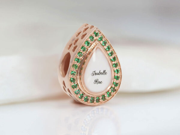 breastmilk charm bead in teardrop shape with emerald birth month crystals around the breastmilk fill with the name in the middle from keepsakemom