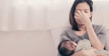 Tired mom holding newborn on couch