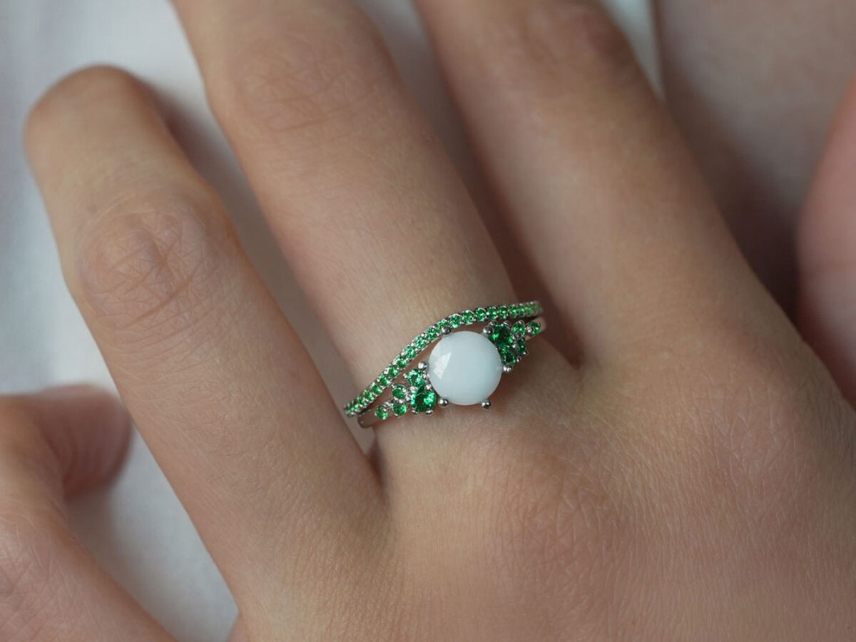 breastmilk jewelry ring on a model hand close-up in rose gold with crystals of birth color emerald