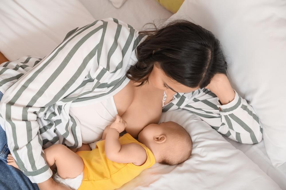 Mom feeding her baby from one breast in bed