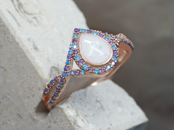 breastmilk ring with drop shaped central breastmilk stone with light blue and purple gems as halo around the stone and around the ring band alternating from keepsakemom in rose gold setting