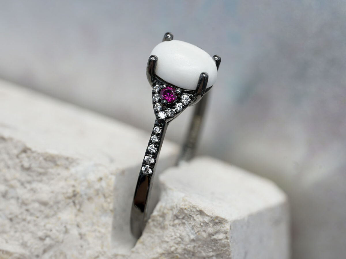 breastmilk ring in rare black setting rhodium or black gold with central breast milk stone in shape of oval and ruby and clear birth month color gems and stones on a band from keepsakemom