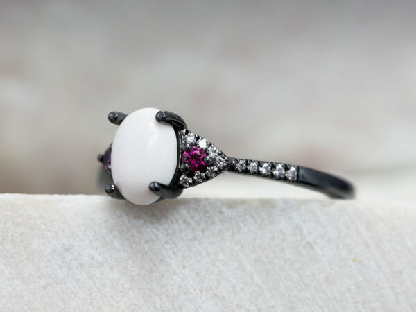 breastmilk ring in rare black setting rhodium or black gold with central breast milk stone in shape of oval and ruby and clear birth month color gems and stones on a band from keepsakemom