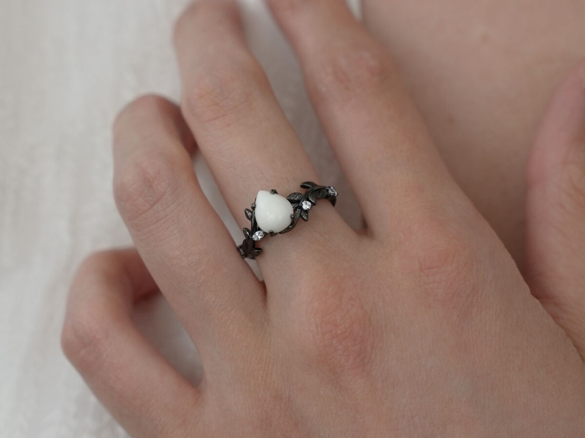 breastmilk ring in rare black setting rhodium or black gold with central breast milk stone in shape of domed drop and clear diamonds birth month color gems and stones on a band from keepsakemom on model hand