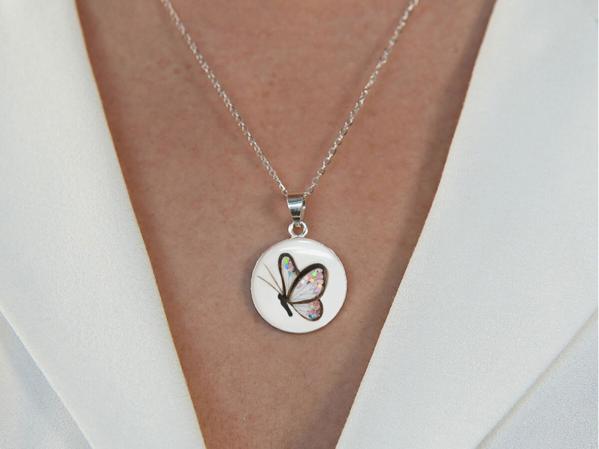 breastmilk disc sterling silver necklace with butterly made with locks of hair of newborn and colored flakes inside on model chest