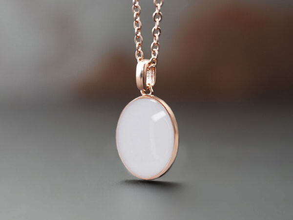 breastmilk jewelry oval simple classic necklace filled with milk. keepsake in rose gold metal cup and chain on dark background from keepsakemom