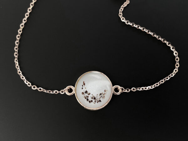 memorial keepsake jewelry disc bracelet filled with breastmilk and crescent moon shaped ashes sprinkled on top in rose gold setting in a box with black background from keepsakemom
