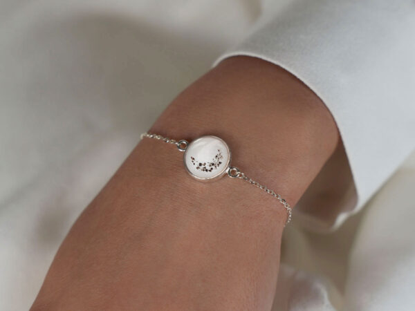 memorial keepsake jewelry disc bracelet filled with breastmilk and crescent moon shaped ashes sprinkled on top in rose gold setting on a model hand from keepsakemom
