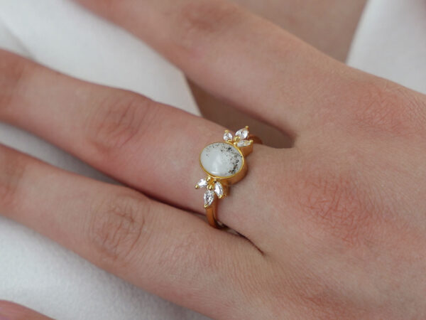 memorial cremation ring with oval breastmilk stone and three crystals on each side with ashes on a model hand, adorned with clear crystals in rose gold filled with breastmilk and ashes and lock of hair from keepsakemom