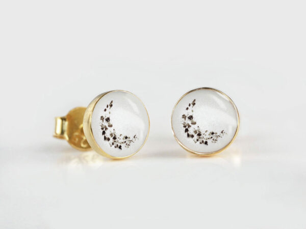 memorial jewelry a pair of yellow gold disc earrings with crescent moon shaped ashes layered on white backdrop of breast milk filled cups from keepsakemom