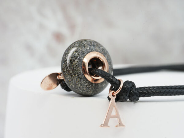 memorial bracelet for a horse owner made from pet's ashes with rose gold cores, the bead is on a black cord with the animal's name initial from keepsakemom