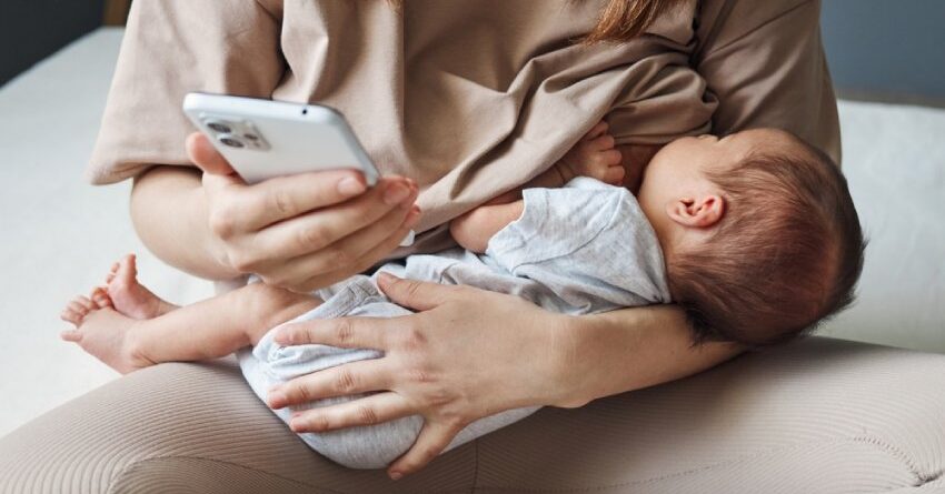 A mom breastfeeding her baby and looking at her phone