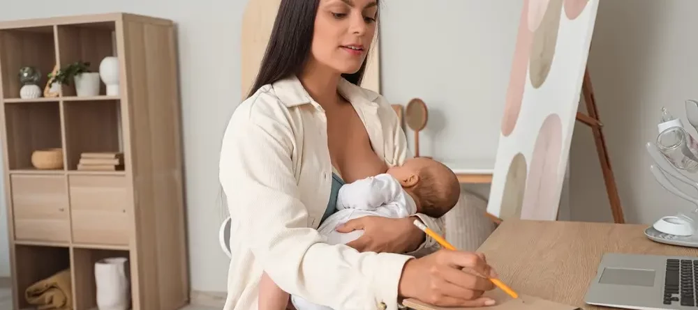 A mother breastfeeding her baby while writing in a notebook