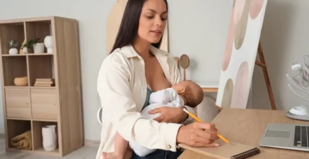 A mother breastfeeding her baby while writing in a notebook