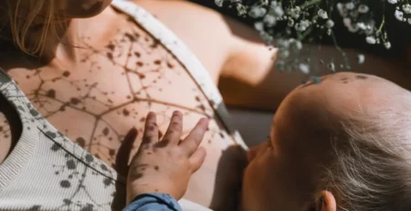 Shadow of flowers atop a mother with a baby on her chest.