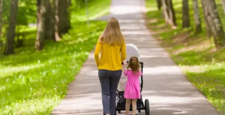 A mother and her toddler daughter take an infant for a walk in a stroller.